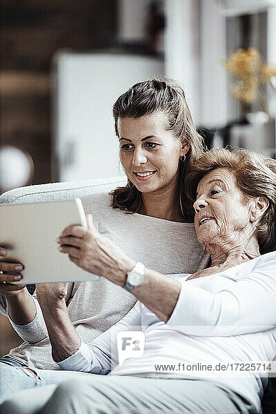 Ältere Frau verwendet digitales Tablet  während sie sich bei ihrer Enkelin zu Hause entspannt