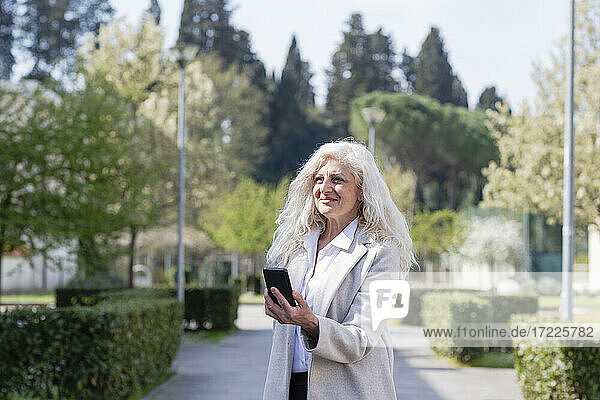 Lächelnde Frau mit Mobiltelefon  die in den Park blickt
