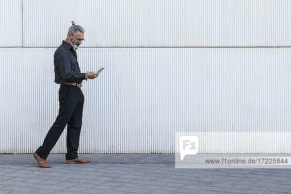 Männlicher Berufstätiger  der ein Smartphone benutzt  während er auf dem Gehweg geht