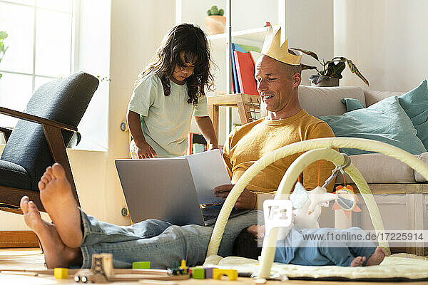 Töchter spielen zu Hause beim arbeitenden Vater mit Papierkrone auf dem Kopf