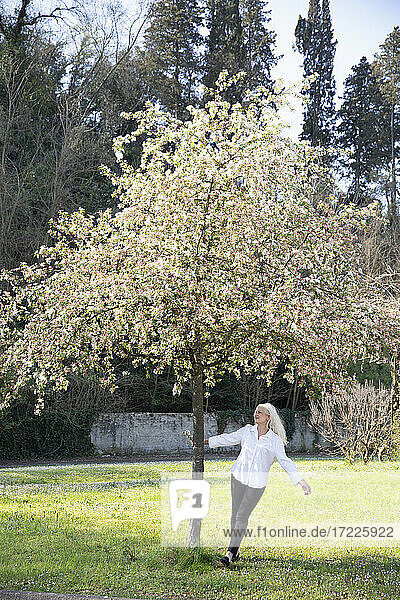 Mature woman walking around tree with flowers at park during springtime