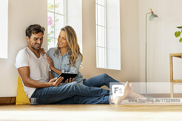 Schöne Frau sieht ihren Freund an  der ein digitales Tablet benutzt  während er zu Hause auf dem Boden sitzt