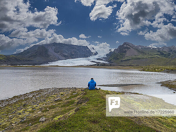 Mittlerer erwachsener Mann mit Blick auf die Aussicht  während er vor einer Lagune sitzt  Breidamerkurjokull-Gletscher