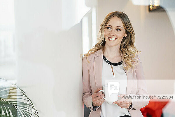 Smiling female professional looking away while holding coffee mug in office