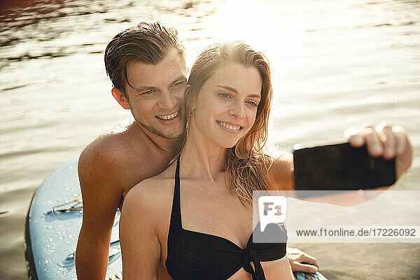 Junges Paar macht Selfies  sitzt auf einem Paddelbrett auf dem See