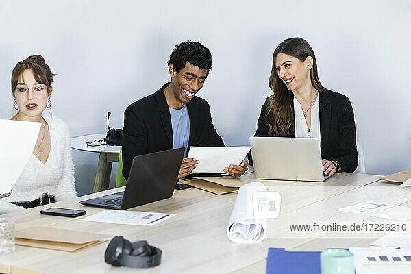 Junge Geschäftsleute  die lächelnd neben ihren Kollegen in einer Besprechung sitzen