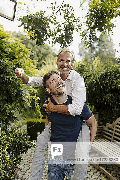 Cheerful son giving piggyback ride to father in backyard