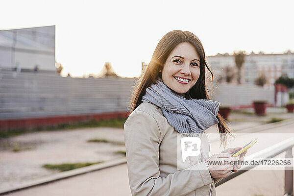 Smiling woman with mobile phone standing at railroad station
