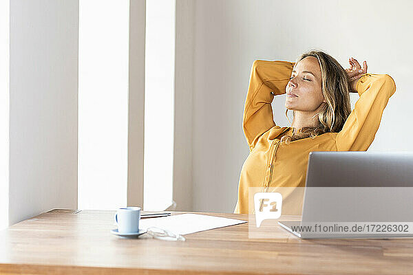 Geschäftsfrau mit Händen hinter dem Kopf  die sich im Büro zu Hause entspannt