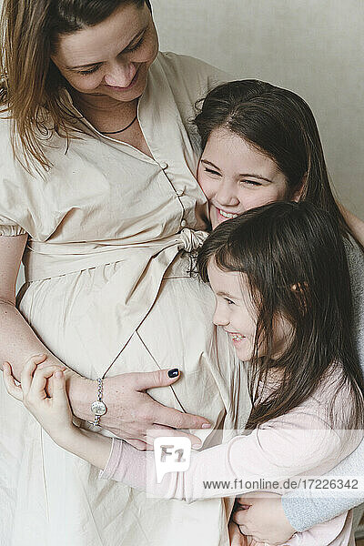 Happy girls embracing pregnant mother at home