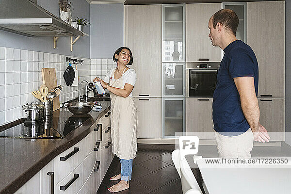 Smiling wife talking to husband while preparing food in kitchen at home