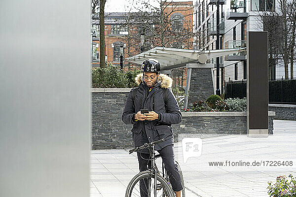 Junger Mann mit Fahrrad und Smartphone auf dem Gehweg