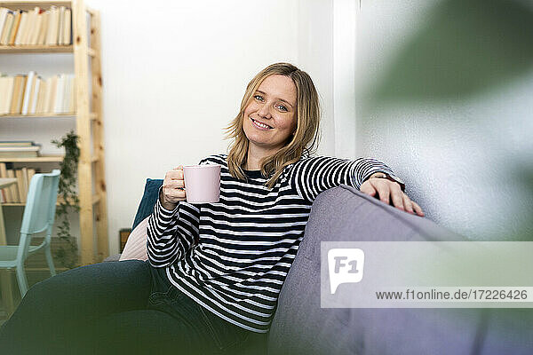 Lächelnde Frau mit Kaffeetasse auf dem Sofa zu Hause