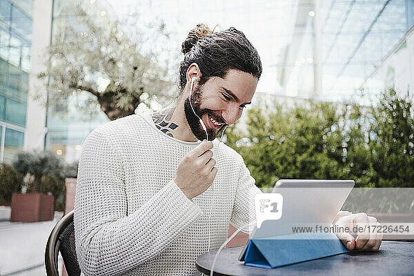 Lächelnder Mann  der einen Videoanruf über ein digitales Tablet in einem Straßencafé führt