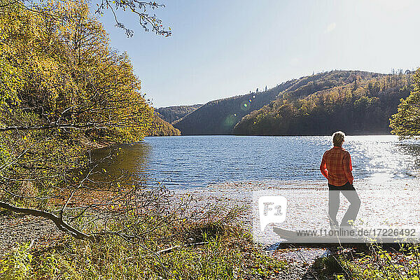 Woman standing on shore of Rursee reservoir on sunny autumn day