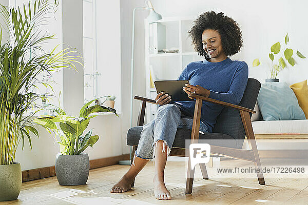 Junge Frau benutzt ein digitales Tablet  während sie zu Hause auf einem Sessel sitzt