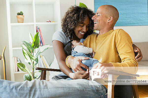 Glückliche Eltern mit schlafendem Baby  das lachend zu Hause sitzt