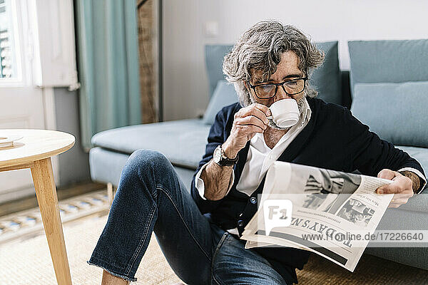 Älterer Mann trinkt Kaffee und liest Zeitung  während er zu Hause sitzt