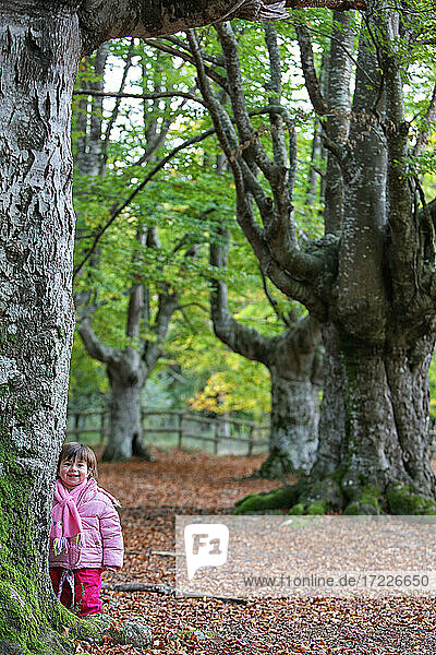 Niedliches Mädchen  das lächelnd an einem Baum im Naturpark Gorbea steht