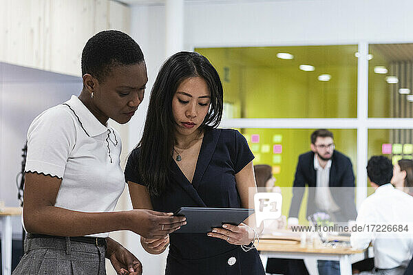 Geschäftsfrau arbeitet an einem digitalen Tablet mit Kollegen im Hintergrund im Büro