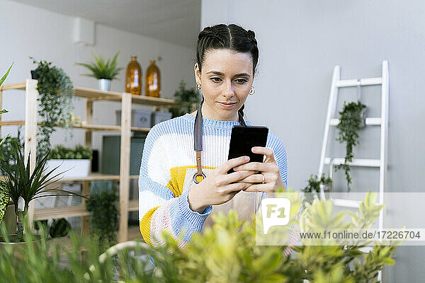 Schöne Frau fotografiert Pflanzen mit dem Handy in einer Werkstatt