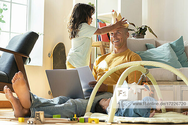 Kleinkind  das seinem Vater eine Papierkrone auf den Kopf setzt  während es von zu Hause aus arbeitet