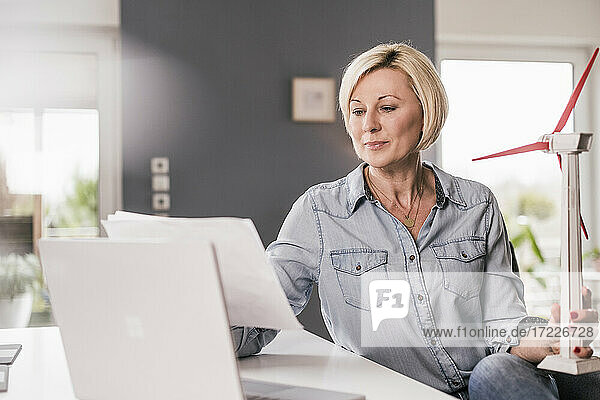 Ältere Geschäftsfrau liest Zeitung und hält ein Windradmodell im Büro