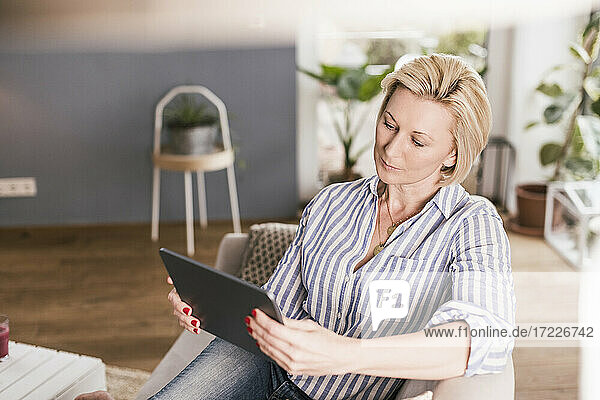 Reife Frau benutzt digitales Tablet  während sie auf dem Sofa im Wohnzimmer sitzt