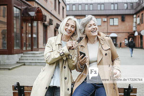 Cheerful female friends listening music while sharing headphones