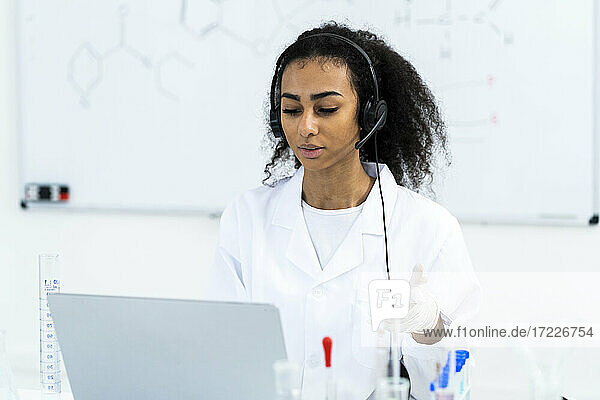 Junge Forscherin mit Headset bei einem Videogespräch über einen Laptop im Labor
