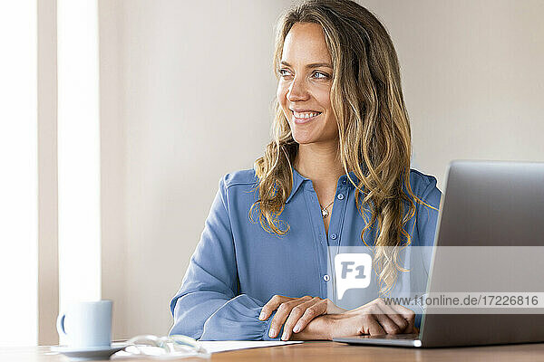 Lächelnde weibliche Fachkraft  die am Schreibtisch im Heimbüro träumt