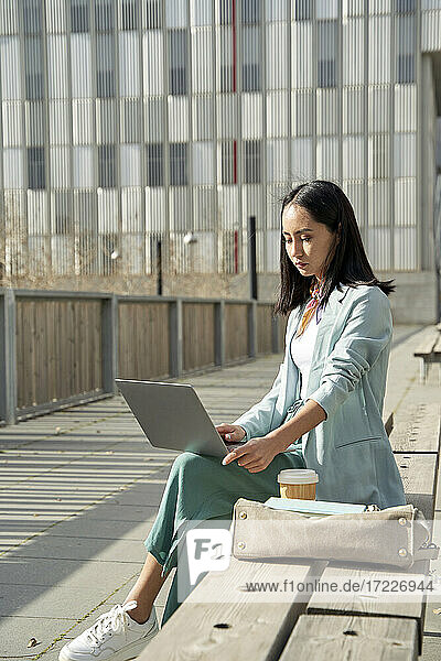 Junge Geschäftsfrau  die einen Laptop benutzt und auf einer Bank sitzt