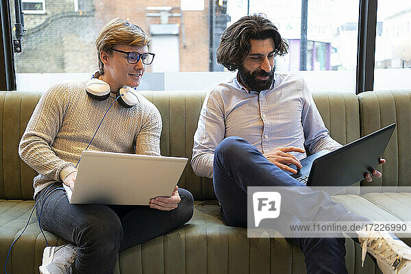Männliche Unternehmer arbeiten am Laptop  während sie auf dem Sofa im Coworking-Büro sitzen