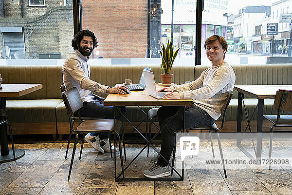Happy male entrepreneurs with laptop sitting at desk in office