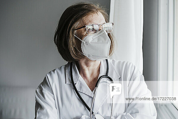 Ältere Ärztin mit Gesichtsschutzmaske  die wegschaut  während sie im Krankenhaus steht