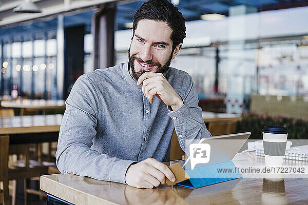 Lächelnder männlicher Unternehmer mit digitalem Tablet und Kreditkarte am Arbeitsplatz
