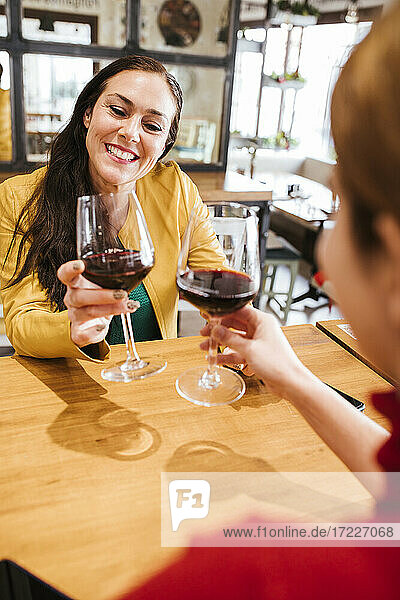 Smiling woman toasting wine glasses with female friend in bar
