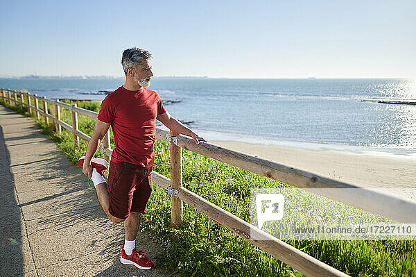 Mann streckt sich in der Nähe des Geländers am Strand an einem sonnigen Tag am Meer