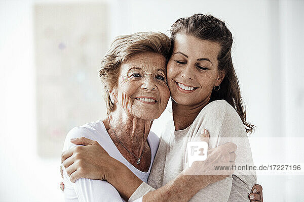 Caring young woman hugging grandmother at home