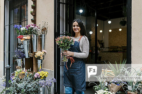Young female florist holding flower vase while standing at shop
