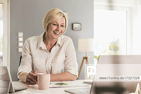 Smiling businesswoman on video call through laptop while having coffee at home