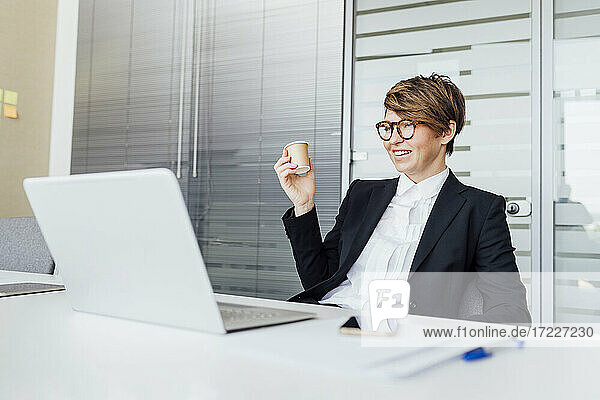 Lächelnde Geschäftsfrau  die einen Kaffee trinkt und auf einen Laptop am Schreibtisch schaut