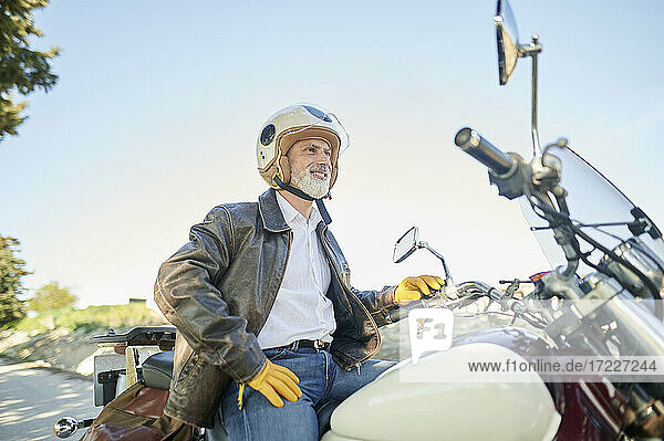 Lächelnder Mann  der auf einem Motorrad sitzend wegschaut