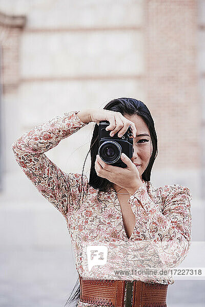 Woman photographing through analog camera by wall