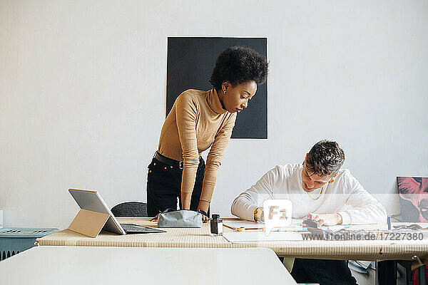 Junge Frau betrachtet einen Mann  der mit einem Füllfederhalter schreibt  während er an einem Tisch im Studio sitzt