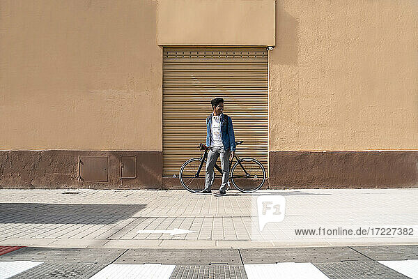 Lächelnder Mann mit Fahrrad  der wegschaut  während er an der Wand steht