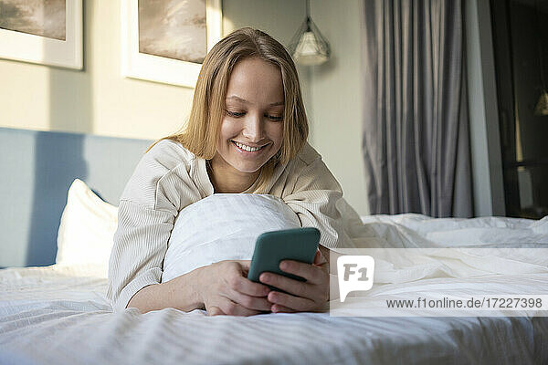 Lächelnde Frau  die ein Mobiltelefon benutzt  während sie auf dem Bett liegt
