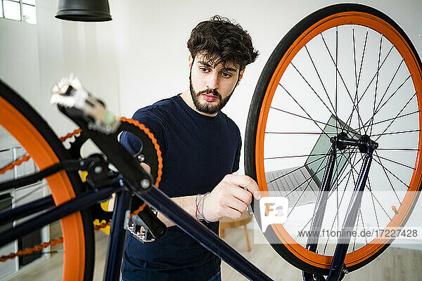 Handsome man with laptop examining wheel alignment of bicycle at home