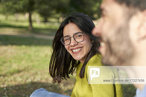 Fröhliche Frau mit Brille sieht ihren Freund an  während sie sich in einem öffentlichen Park amüsiert