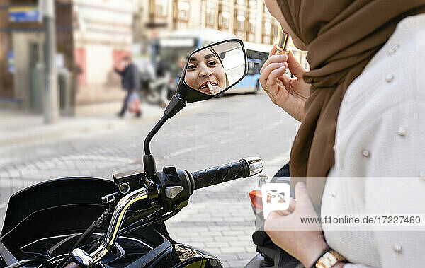 Junge Frau trägt Lippenstift auf und schaut in den Motorradspiegel